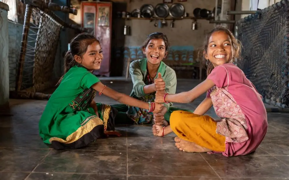 Drei Kinder sitzen lachend auf dem Boden. | © UNICEF/UN0378258/PANJWAN Das Foto zeigt drei Geschwister in Surat District in Gujarat State, Indien.