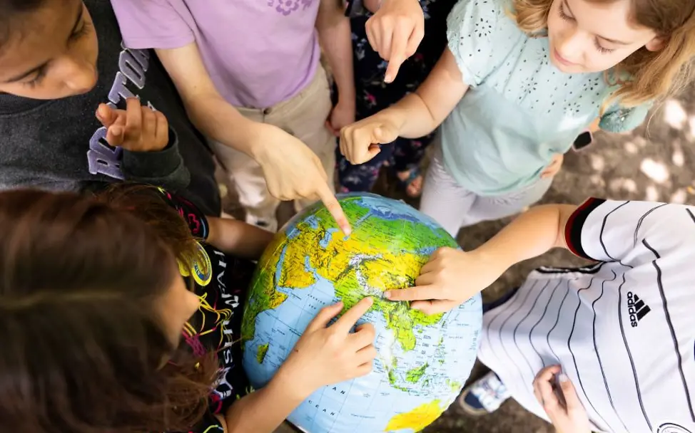 Kinderfreundliche Kommunen: Kinder erkunden Karten | © UNICEF/Etges Mehrere Kinder stehen im Kreis und zeigen auf einen Globus.