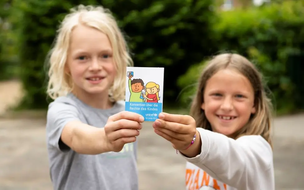 Kinderfreundliche Kommunen: Kinder zeigen Ihnen eine Karte zu Kinderrechten. | © UNICEF/Etges Zwei Kinder halten eine Broschüre zu Kinderrechten in die Kamera
