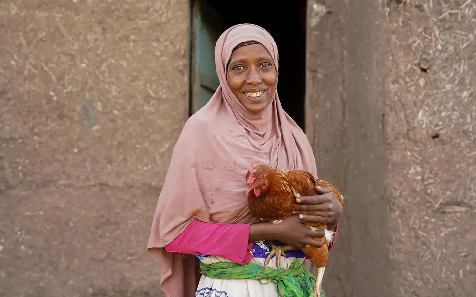 Ein Huhn, das mehr bedeutet: lokale Geflügelhaltung stärkt Ernährung, Gesundheit und Bildung. |© UNICEF//Asrat Eine Frau hält ein Huhn auf dem Arm und blickt in die Kamera