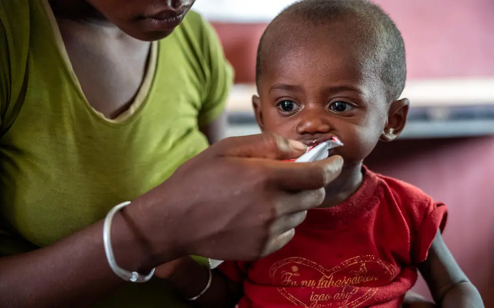 Erdnusspaste bietet schnelle, unkomplizierte Hilfe für mangelernährte Kinder. | © UNICEF/Andrianantenaina Was ist Erdnusspaste: Ein Baby bekommt Erdnusspaste auf dem Schoß seiner Mutter.