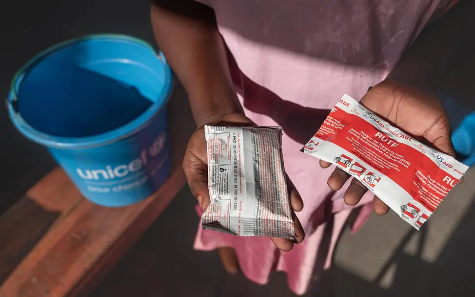 Erdnusspaste kann direkt verzehrt werden und ist auch ungekühlt lange haltbar. | © UNICEF/Andrianantenaina Was ist Erdnusspaste: Verpackte Erdnusspaste in Kinderhänden