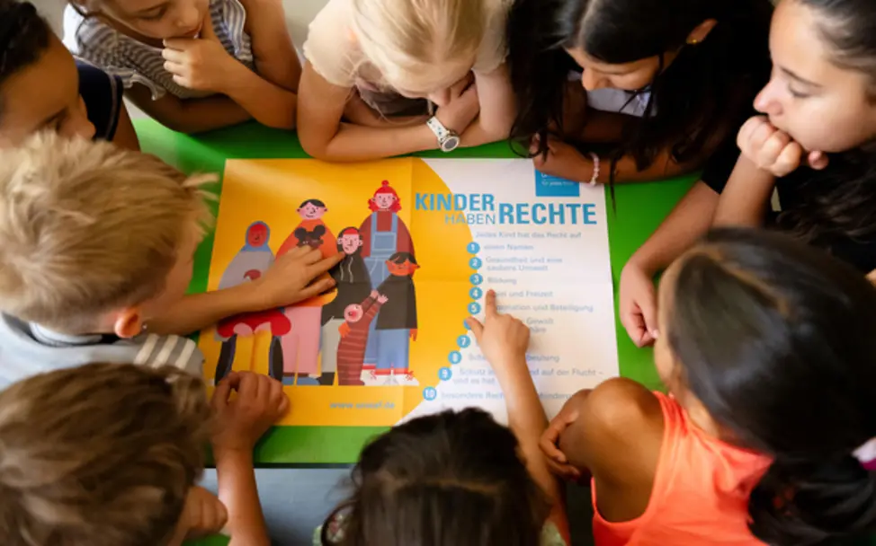 Kinder einer UNICEF-Kinderrechteschule schauen ein Kinderrechteplakat an. | © UNICEF/Etges Kinderfreundliche Kommunen: Kinder einer UNICEF-Kinderrechteschule schauen ein Kinderrechteplakat an.