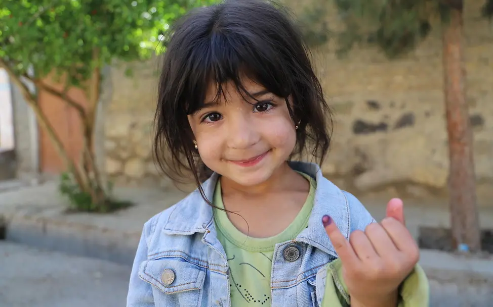 Ein Mädchen in Afghanistan nach ihrer Polio-Schluckimpfung | © UNICEF/UNI995937/ Polio Impfung: Ein Mädchen zeigt nach ihrer Schluckimpfung gegen Kinderlähmung die Markierung an ihrem Finger.