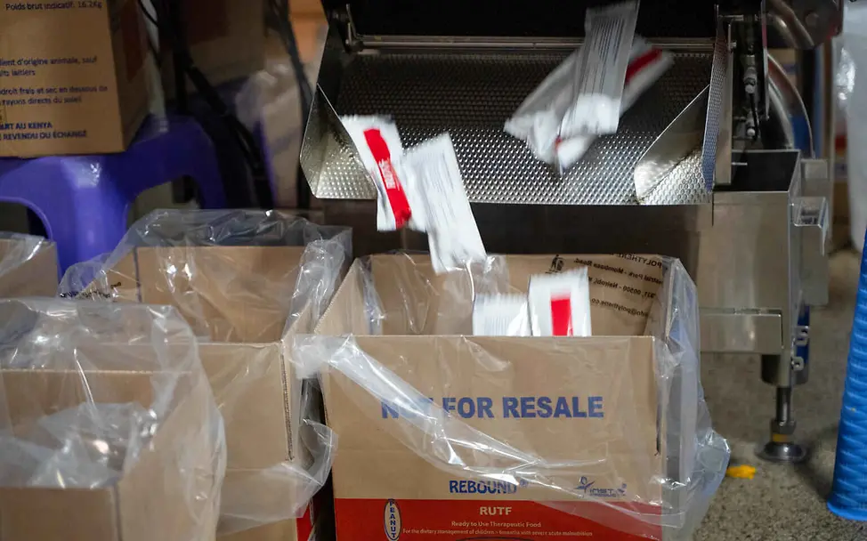 Erdnusspaste ist sicher verpackt, lange haltbar und leicht zu portionieren. | © UNICEF/Ekwam Erdnusspaste Herstellung: Beutel mit Erdnusspaste fallen aus einer Verpackungsmaschine in einen Karton.