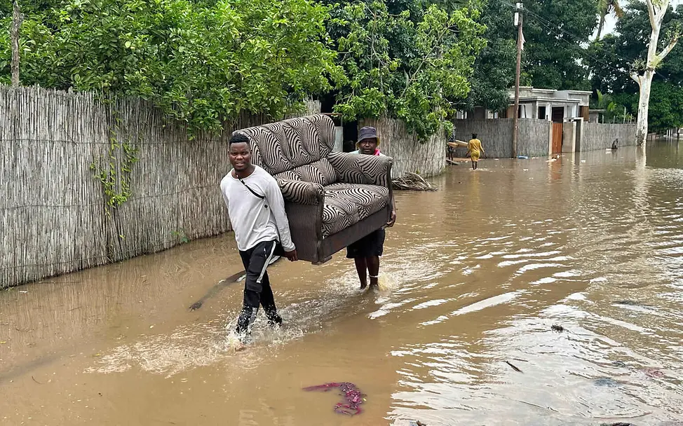 Folgen von Hochwasser: Zwei Männer tragen ein Sofa eine überschwemmte Straße entlang.