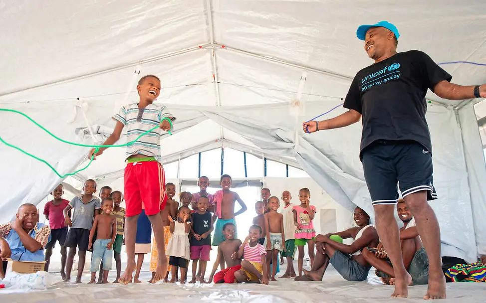 Folgen von Hochwasser: Ein Junge und ein UNICEF-Mitarbeiter springen Seil im Schulzelt.