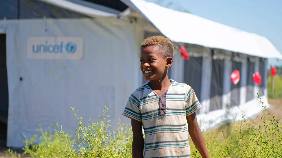 Folgen von Hochwasser: Ein Junge steht lächelnd vor einem UNICEF-Schulzelt.