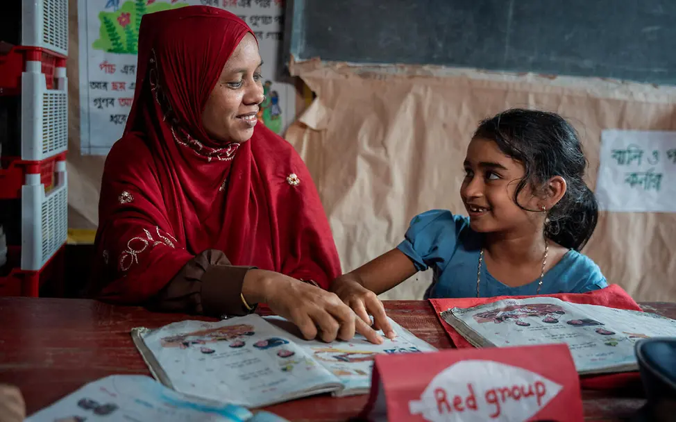 Mit Aus- und Fortbildungsangeboten für Lehrkräfte hilft UNICEF, damit Kinder in Bangladesch eine bessere Chance auf Bildung haben. | © UNICEF/Himu Bildung in Bangladesch: Eine Lehrerin und eine Schülerin sitzen gemeinsam am Tisch und schauen sich ein Schulbuch an.