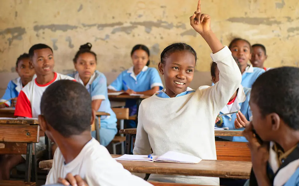 Viele Eltern in Madagaskar können sich keine Schulbildung für ihre Kinder leisten. | © UNICEF/Ramasomanana Bildung in Madagaskar: Eine Schülerin meldet sich im Klassenzimmer mit anderen Schulkindern.