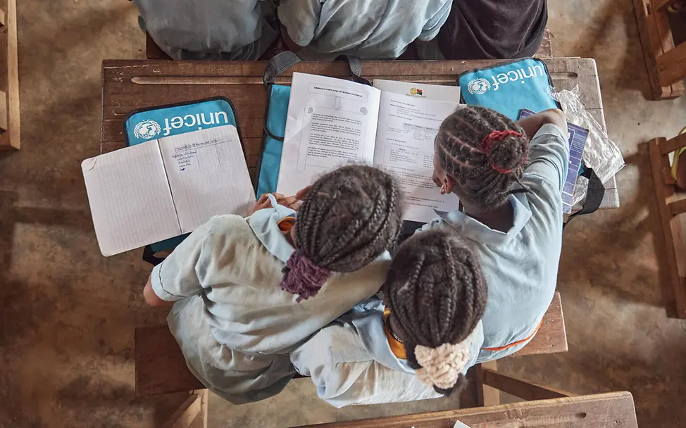 Gemeinsames Lernen hilft den Mädchen in Madagaskar, wieder in den Schulalltag zurückzufinden. | © UNICEF/Andriantsoarana Bildung in Madagaskar: Drei Mädchen sitzen über einen Schultisch gebeugt und lernen in einem Arbeitsbuch.
