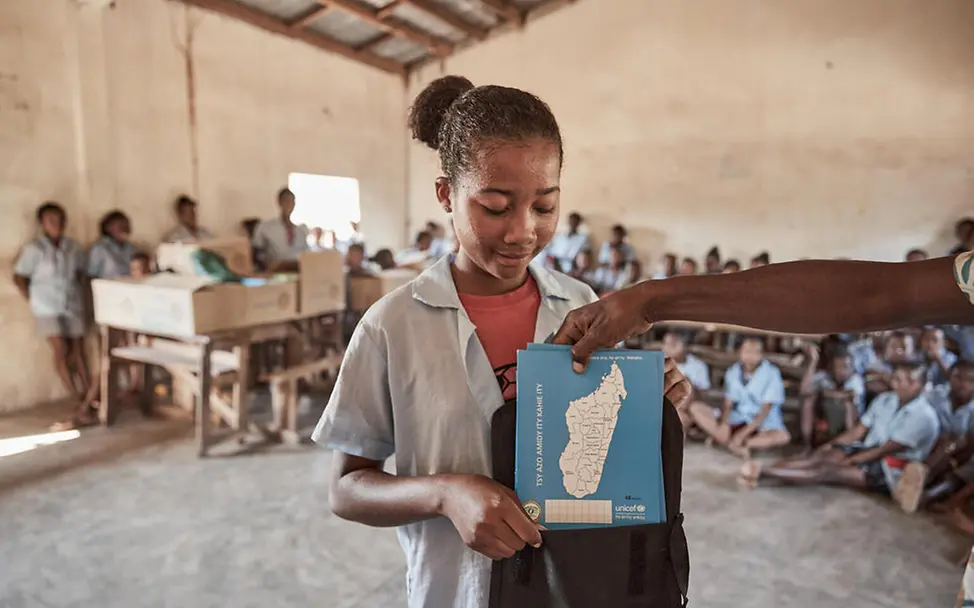 Let Us Learn UNICEF: Eine Schülerin steht vor ihrer Klasse und bekommt Schulhefte.