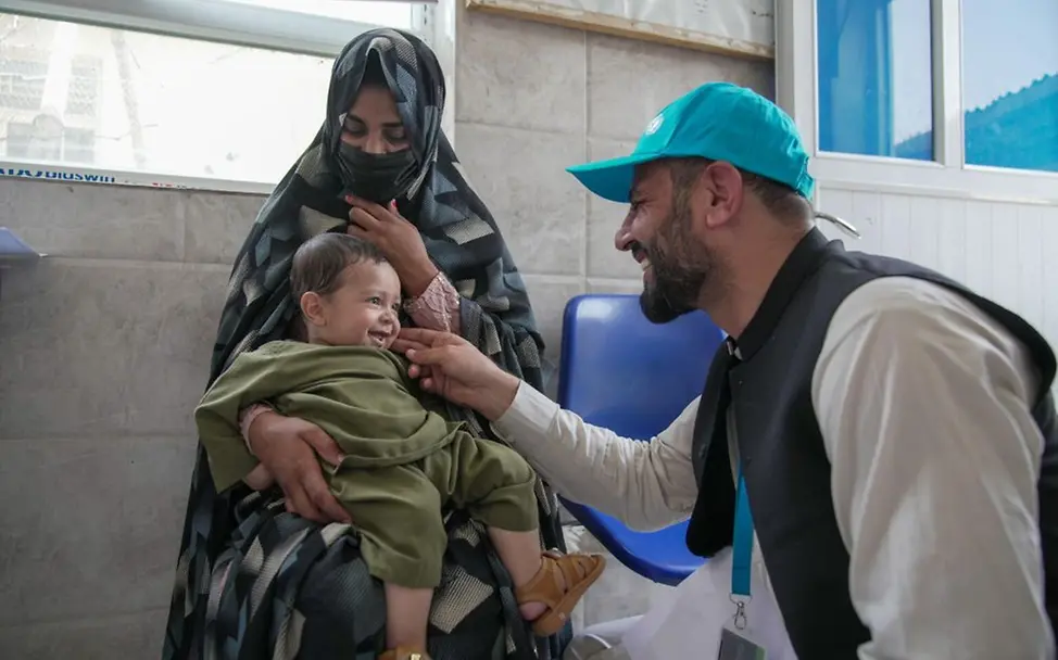 © UNICEF/Karimi Ein UNICEF-Helfer sitzt vor einem Kind, das auf dem Schoß seiner Mutter sitzt.