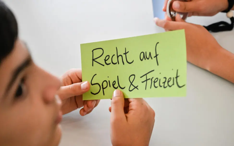 Junge hält einen Zettel, auf den er "Recht auf Spiel und Freizeit" geschrieben hat.