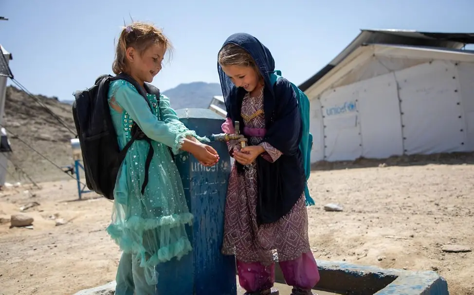 Asiya (6) und Sumaya (7) waschen sich die Hände. | © UNICEF/Meerzad Kindheit in Afghanistan: Asiya (6) and Sumaya, (7) stehen vor einem UNICEF-Zelt und waschen sich die Hände mit sauberem Wasser.